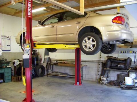 1974 Dodge Challenger - A gold sedan is raised on a red and yellow car lift in a workshop setting.
