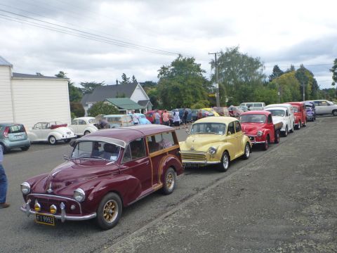 1969 MINI Cooper - Several vintage cars are lined up on the side of the road under a cloudy sky.
