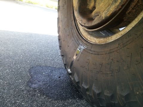 1988 Ford Bronco - Tire repair patch visible on a vehicle tire. A dark fluid stain is on the road surface.