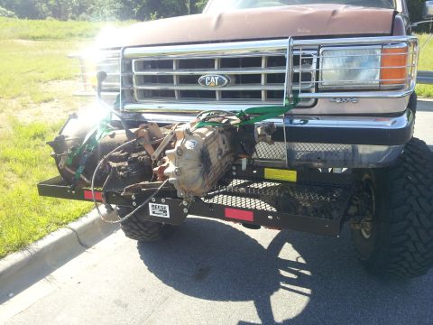 1988 Ford Bronco - A Ford truck is equipped with a front cargo carrier holding a transmission, secured with straps.