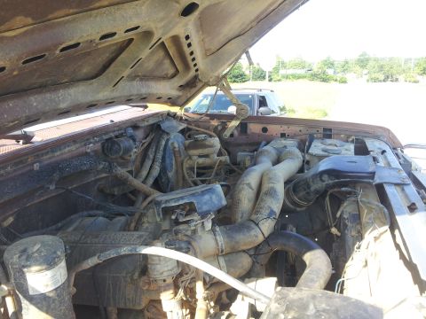 1988 Ford Bronco - The engine bay of a weathered brown truck, likely from the 1980s, is visible with the hood raised.