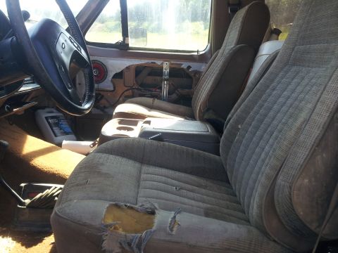 1988 Ford Bronco - The interior of the truck shows significant wear and tear on the seats, with a bottle of fluid visible on the floor.