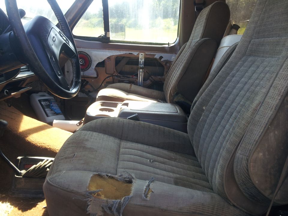 Interior shot of a truck with ripped seats and a bottle of fluid on the floor