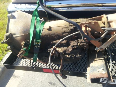 1988 Ford Bronco - A transmission is being transported on a trailer, secured by green straps.