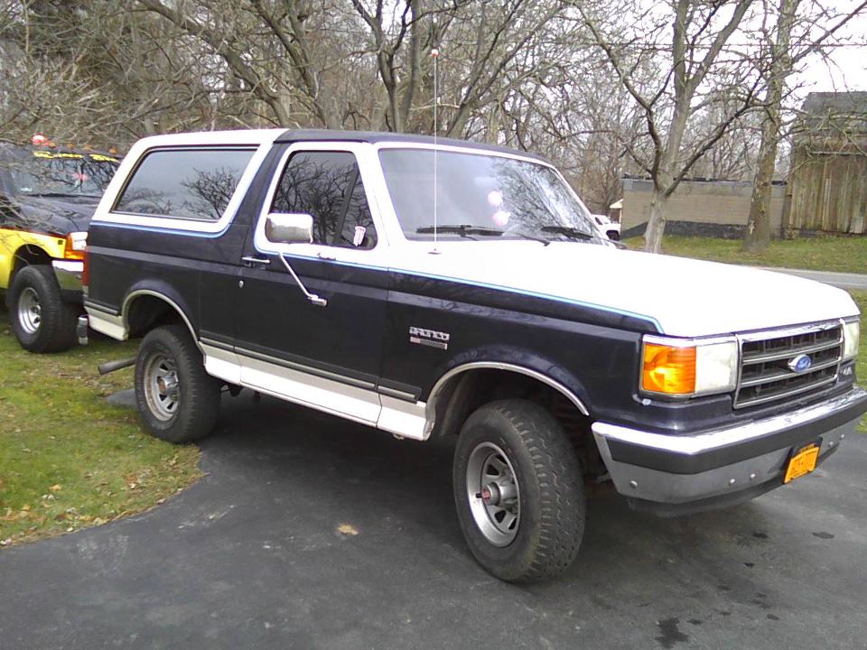 Dark blue and white Ford Bronco parked on asphalt, with a yellow truck partially visible to the left
