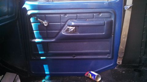 1979 Ford Bronco - Interior view of a blue door panel, showing the window crank and seatbelt.