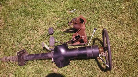 1979 Ford Bronco - Disassembled vehicle parts, including a steering column and pedals, are laid out on a grassy surface.