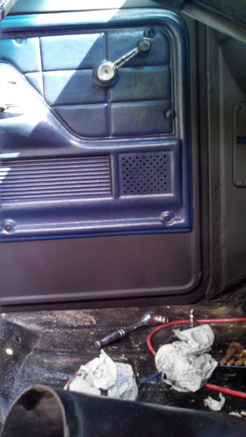 1979 Ford Bronco - The interior door panel of a vehicle shows a window crank and speaker grille, with tools on the floor.