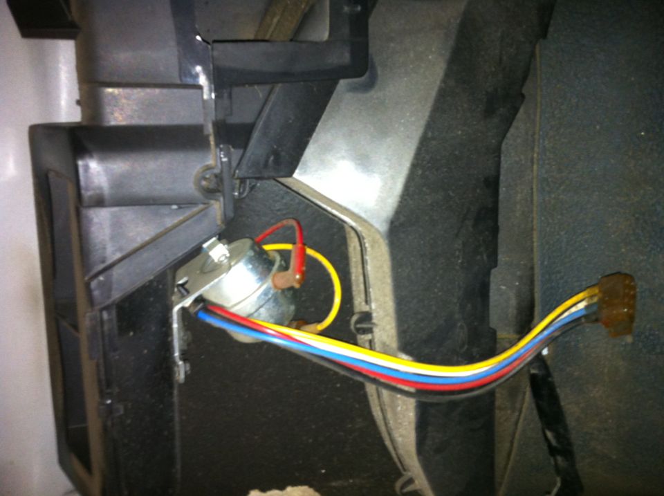 Close-up of a silver switch with red, yellow, blue, and white wires connected, mounted to black plastic interior trim