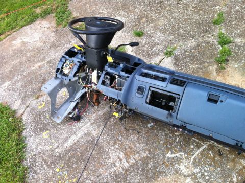 1992 Ford Bronco - A disassembled vehicle dashboard assembly, including the steering wheel and exposed wiring, rests on a concrete surface.