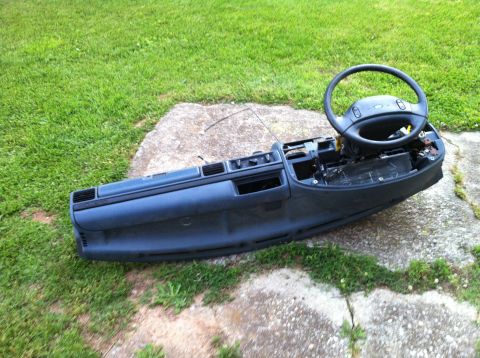 1992 Ford Bronco - Dashboard assembly and steering wheel removed from a vehicle, lying on grass and concrete.