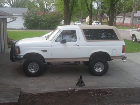 1996 Ford Bronco - Side view of a white Ford Bronco with a tan removable top and lifted suspension.
