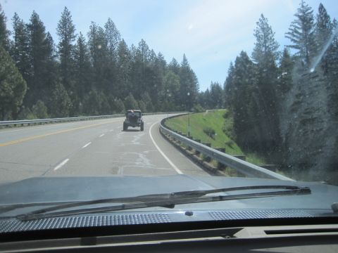 1989 Ford Bronco - A Jeep Wrangler travels down a winding highway surrounded by dense pine forests under a clear sky.