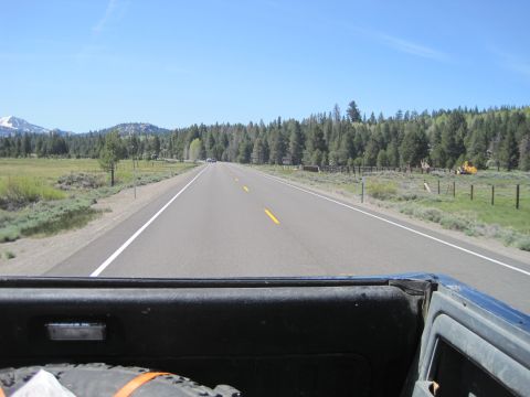 1989 Ford Bronco - Driving down a long, empty highway surrounded by trees and mountains under a clear blue sky.