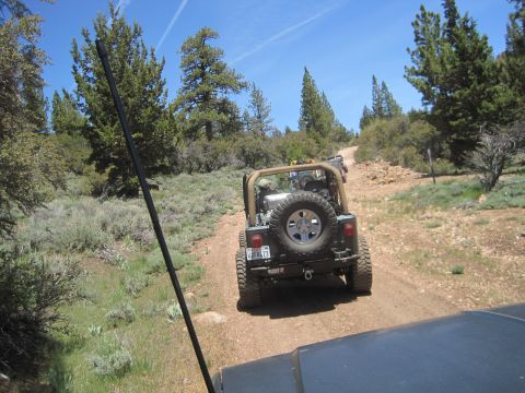 1989 Ford Bronco - Two off-road vehicles navigate a dusty trail through a natural landscape under a clear blue sky.