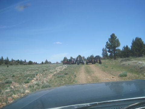 1989 Ford Bronco - A group of off-road vehicles are stopped on a dirt path in a rural landscape under a clear blue sky.