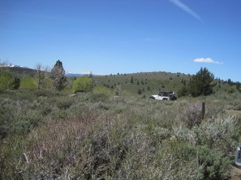1989 Ford Bronco - Two off-road vehicles are parked in a vast, grassy field under a clear blue sky.