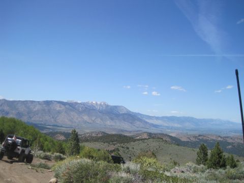 1989 Ford Bronco - Two off-road vehicles navigate a dirt track amidst a scenic landscape of rolling hills and distant mountains.