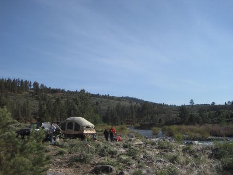 1989 Ford Bronco - A group enjoys a day at a riverside campsite with their vehicles and camping gear.