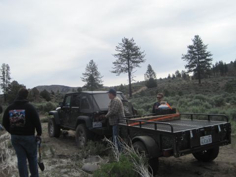 1989 Ford Bronco - A black Jeep Wrangler is hitched to a trailer, with people standing around it in a dry, brushy landscape.