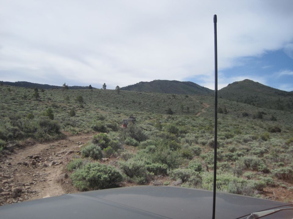 Two off-road vehicles navigate a dusty trail through a scrub-covered hillside