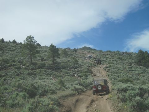 1989 Ford Bronco - Multiple 4x4 vehicles ascend a challenging off-road trail on a dry, brushy slope.