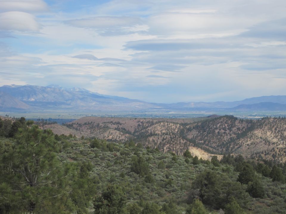 Mountain landscape with rolling hills covered in trees and brush, distant mountains under a cloudy sky