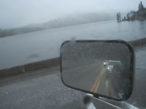 1989 Ford Bronco - Two vehicles are seen through a side mirror on a wet road during foggy weather.