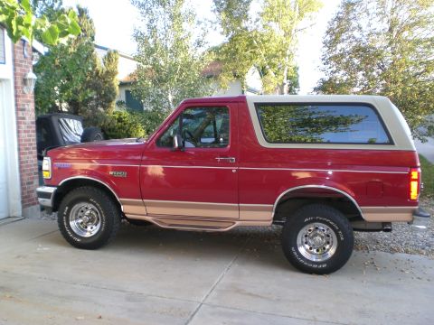 1995 Ford Bronco - This red and tan Ford Bronco is parked on a concrete driveway next to a brick garage.