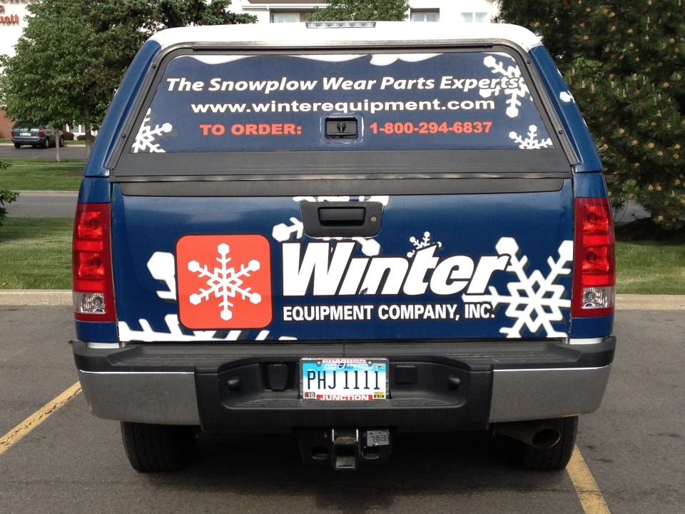 Rear view of blue pickup truck with Winter Equipment Company logos and a camper shell