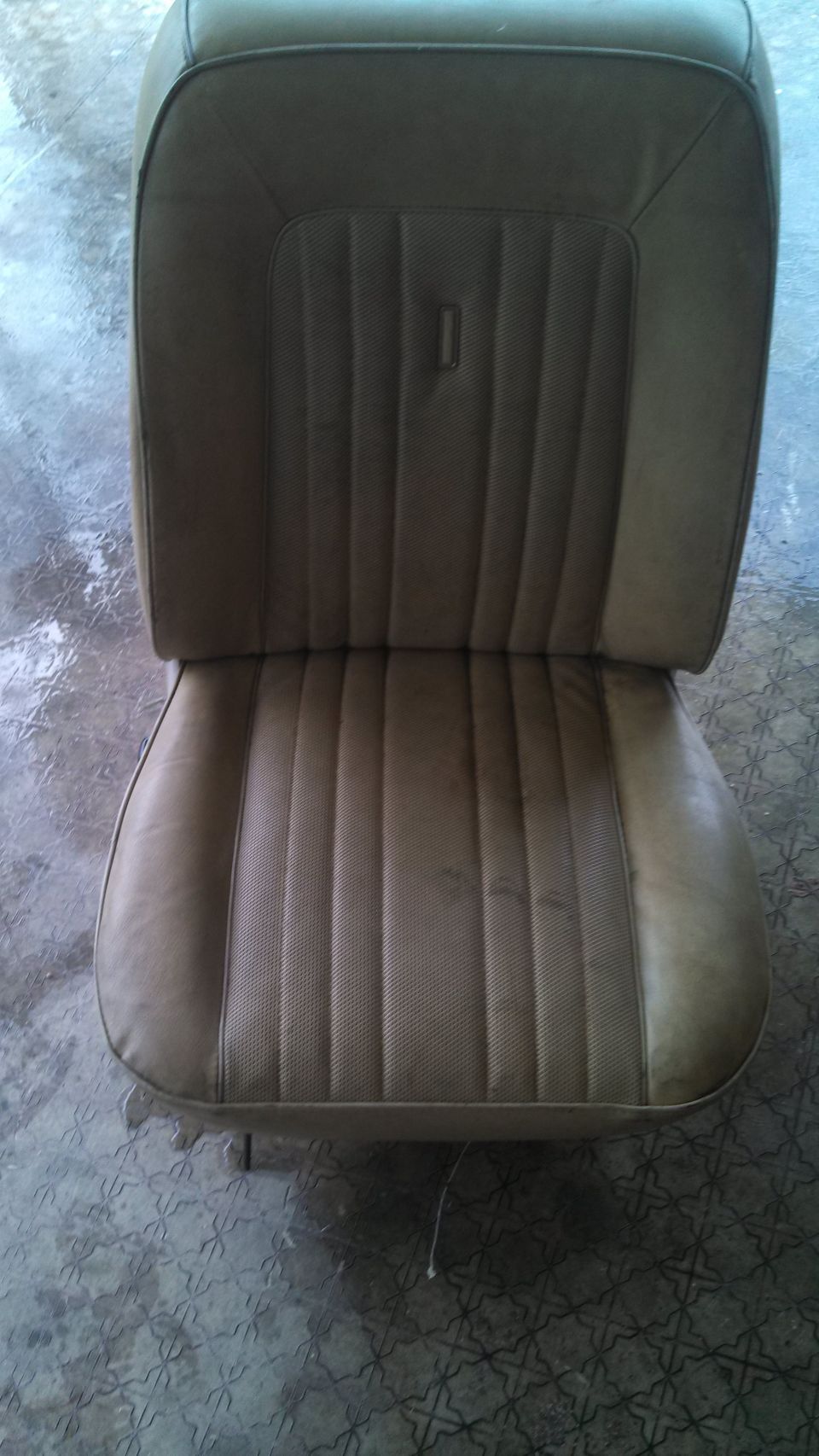 Tan vinyl seat with vertical stitching and a small rectangular emblem on the backrest