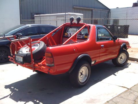 1968 Ford Mustang - A modified red pickup truck with a roll cage and spare tire is parked outdoors next to another vehicle.