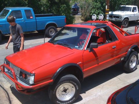 1968 Ford Mustang - Modified red Subaru Brat parked next to a blue Ford pickup truck on a sunny day.