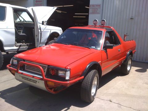 1968 Ford Mustang - A red Subaru Brat is parked next to a white SUV with its hood open.