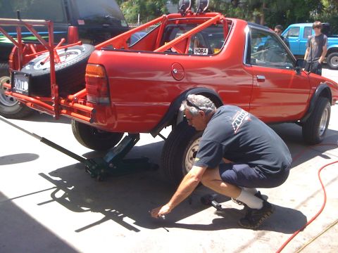 1968 Ford Mustang - A man works on the rear tire of a red coupe utility, which features a custom roll cage and external spare tire mount.