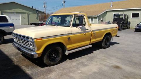 1979 Ford Bronco - This two-tone Ford pickup truck is parked in a lot with other vehicles and buildings in the background.