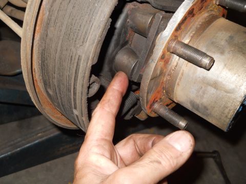 1992 Ford Bronco - A finger points to a part of the brake drum and hub assembly on a vehicle.