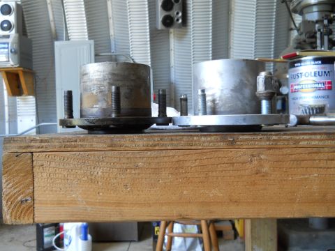 1992 Ford Bronco - Two metal wheel hubs with bolts are displayed on a wooden workbench, with a can of Rust-Oleum in the background.