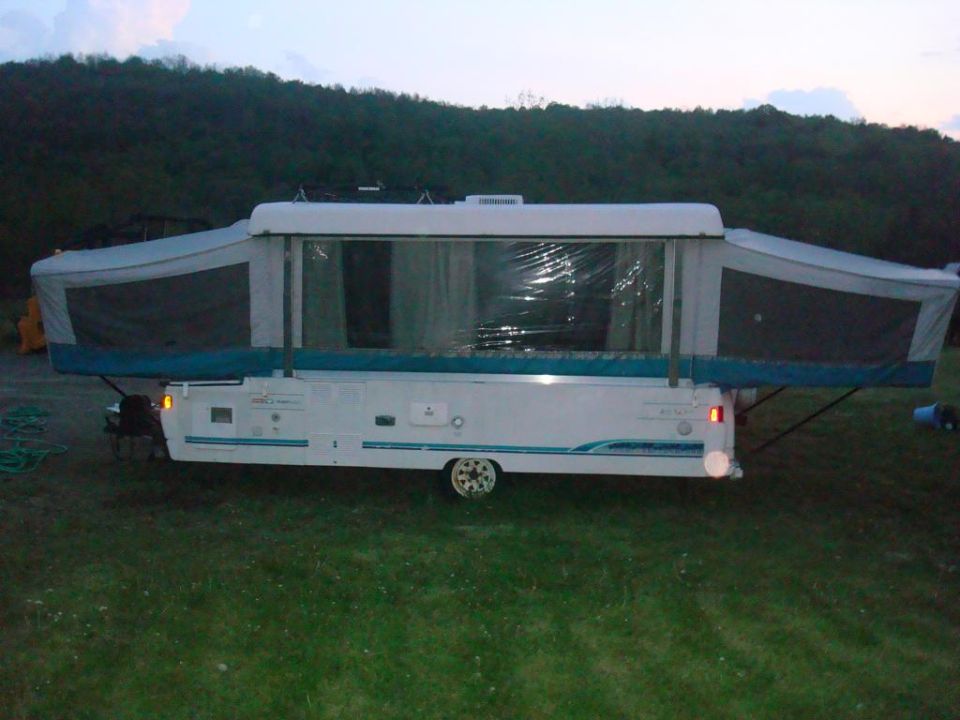 Pop-up camper trailer with sides extended, parked on grass