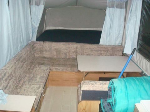 2007 Mazda 6 - The interior of a pop-up camper shows a sleeping area, a U-shaped couch, and a fold-down table.