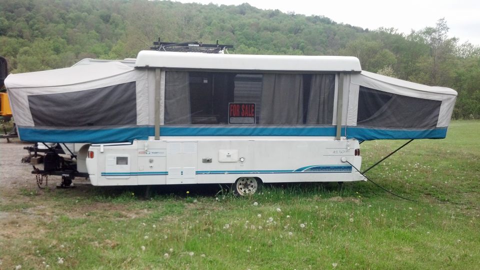 Pop-up camper with blue trim and a 'For Sale' sign in the window