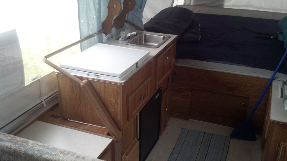 Interior view of a pop-up camper showing a sink, stovetop, and bed area