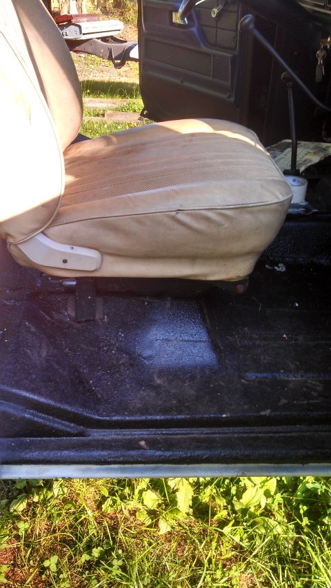 1979 Ford Bronco - The interior of a vehicle shows a tan seat and black floor, with grass visible outside the open door.