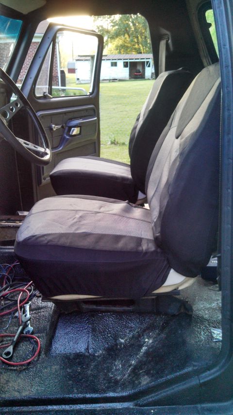 1979 Ford Bronco - The interior of a truck shows seat covers and wiring on the floor, with a view of the outdoors through the open door.
