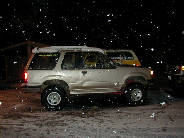 Side view of tan two-door Ford Explorer at night in falling snow with 4x4 decals