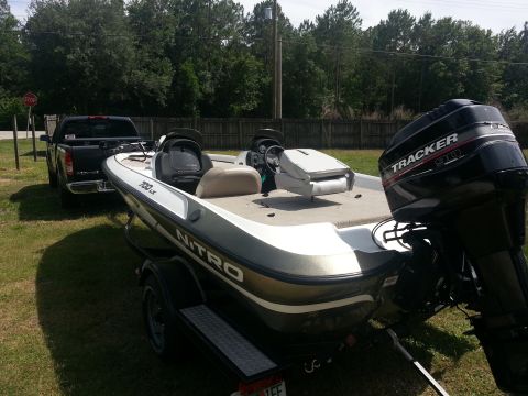 2003 Tracker Tournament - A boat on a trailer is parked next to a pickup truck in a grassy area.