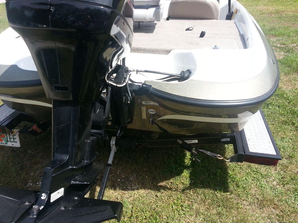 Back of a boat on a trailer with a black outboard motor. Some text is visible on the boat's hull