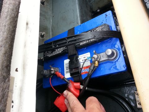 2003 Tracker Tournament - A blue boat battery is secured with a black strap and connected with red and black wires.