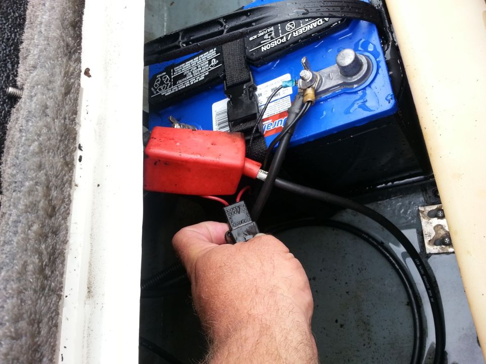 Hand connecting a wire to a boat battery terminal with a red fuse holder