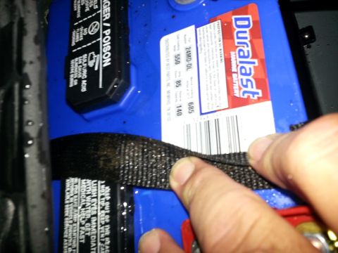 2003 Tracker Tournament - A Duralast car battery is shown with a finger holding down a securing strap.